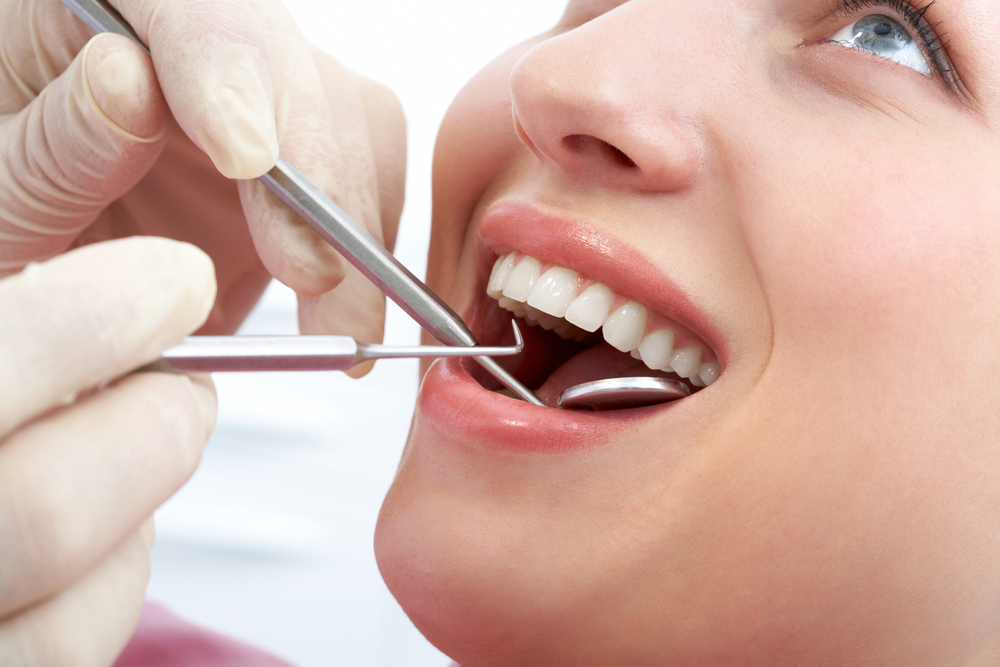 Close-up of patients open mouth during oral inspection with mirror and hook